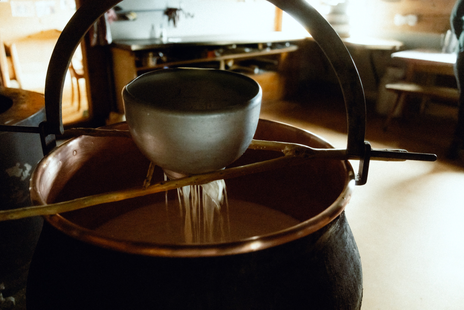 Milch läuft durch ein Siebbehälter ins Kupferkessi